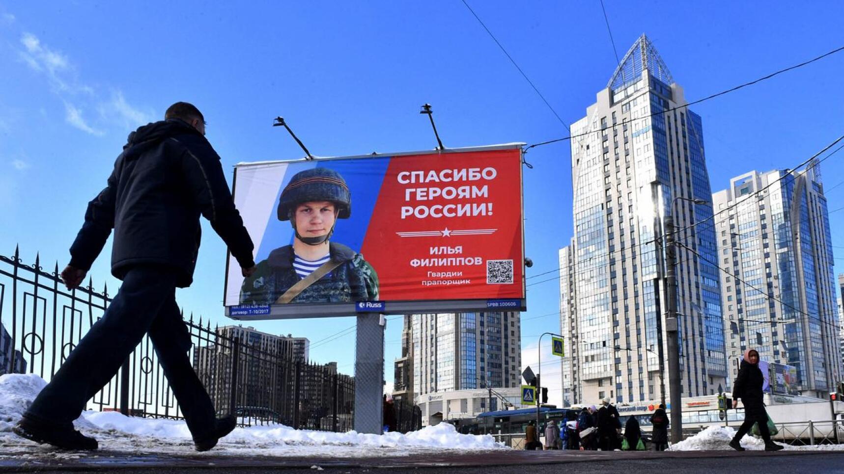 Pietarin kadulla kävelevä mies katselee mainostaulua, jossa on venäläinen sotilas ja iskulause "Kiitos Venäjän sankareille!".