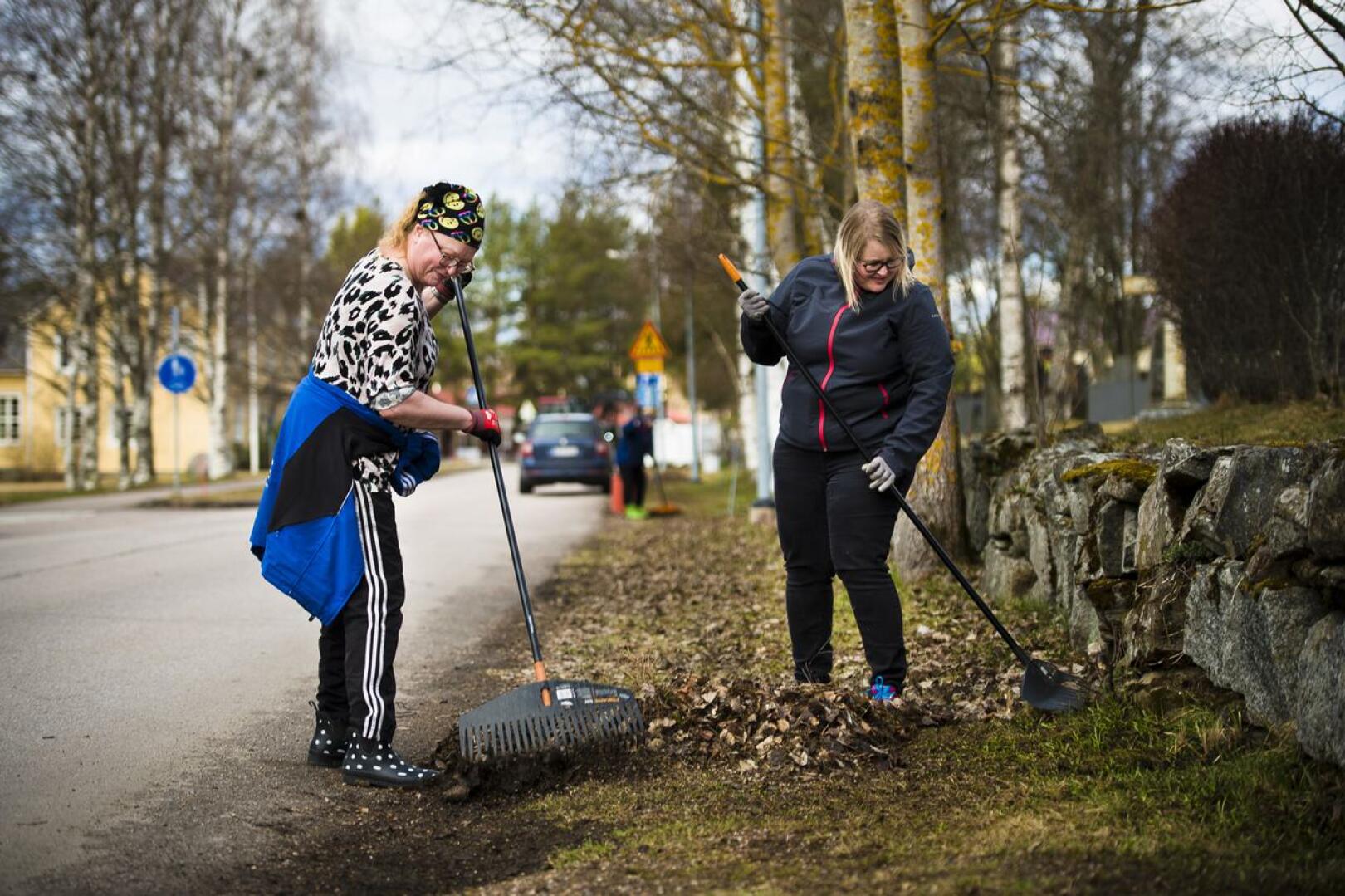 Irja Visuri (vas.) ja Anna-Maria Kumara haravoivat hautausmaan ja Seuratien väliset lehtipatjat kasoiksi traktorin etukuormaajan kauhaan nostamista varten.