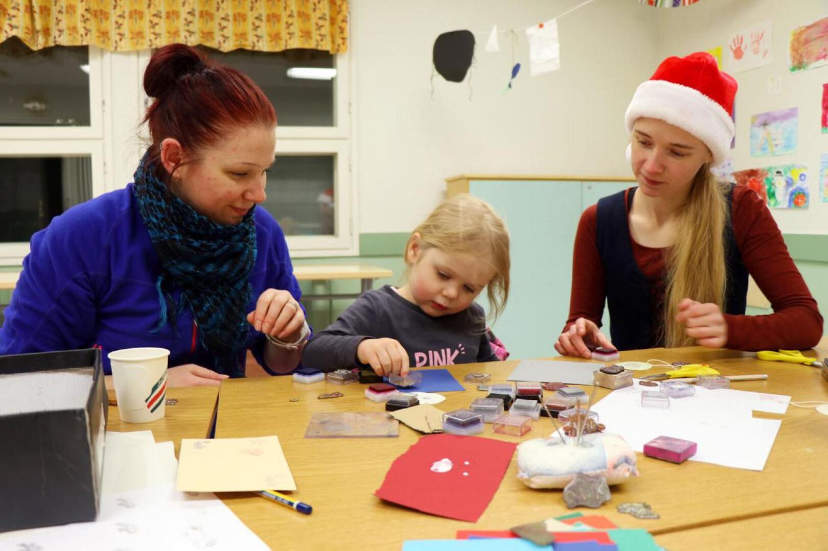 Kolmevuotias Ella Forsbacka (kesk.) keskittyi koristelemaan joulukortteja leimasimella 4H:n järjestämässä joulupajassa. Vieressä äiti Satu Forsbacka (vas.) ja 4H-yhdistyksen toiminnanohjaaja Emilia Känsälä.